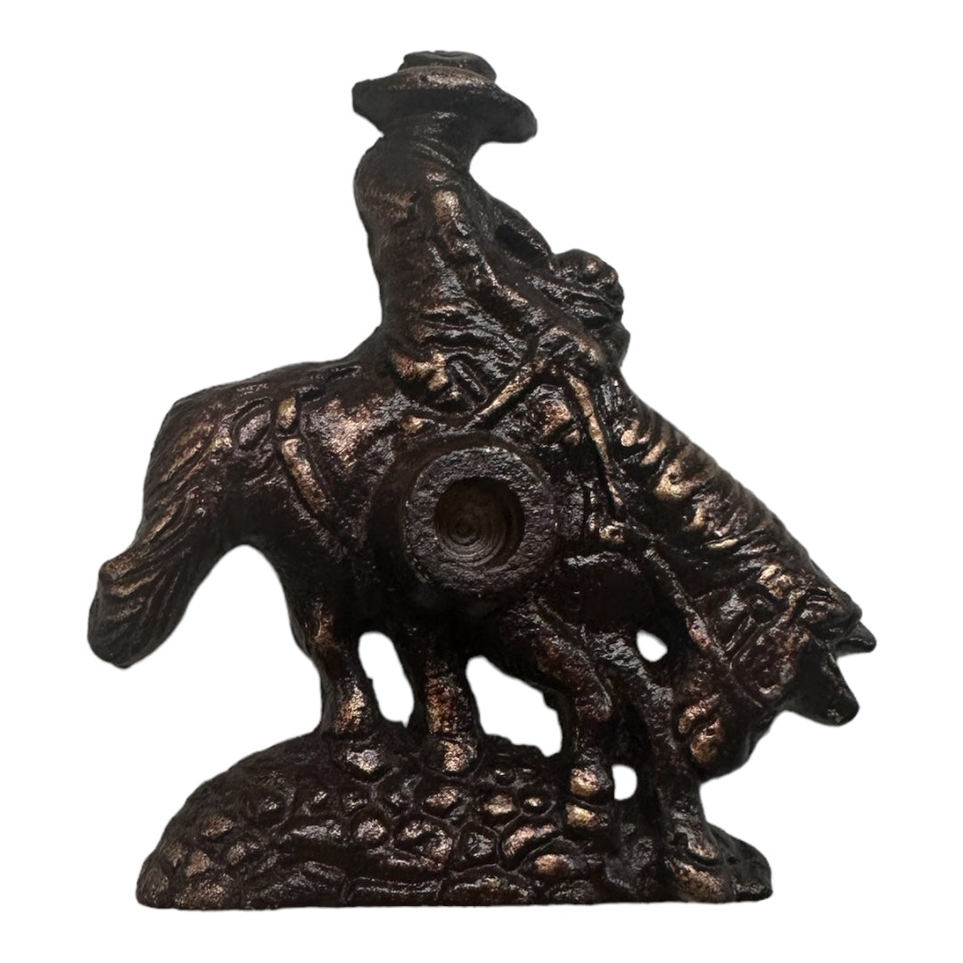 PAINES Bronze Finish Cowboy Holder & 10 Balsam Fir Logs showcases a bronze cowboy riding a horse while wielding a lasso, featuring intricate textures and set on a rugged base. This piece epitomizes the rustic charm of traditional craftsmanship, akin to capturing the essence of frontier life against a white background.