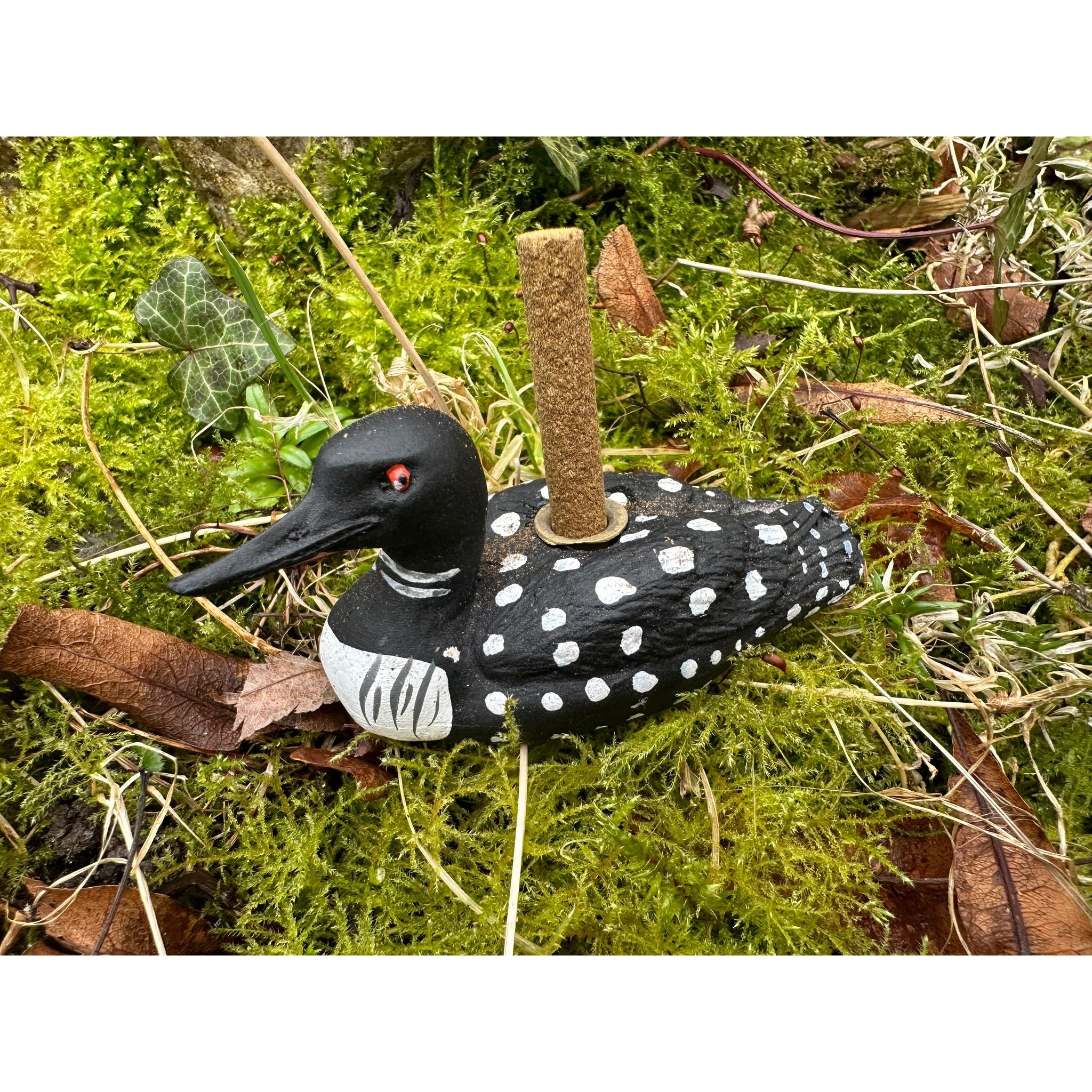 A PAINES Incense Loon Incense Holder, accompanied by 12 Balsam Fir logs, sits on vibrant green moss surrounded by leaves and ivy.