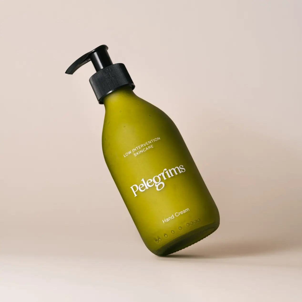 A green bottle of Pelegrims Polyphenol Hand Cream with a black pump dispenser on a white background. The label reads "Low Intervention Skincare" and features English Ortega Grape Extract for rejuvenation.