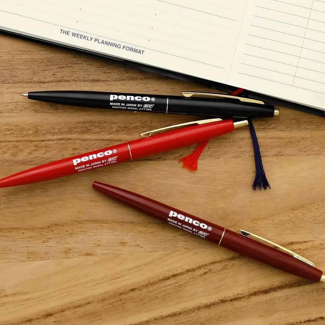 A red Hightide Penco Knock Ballpoint Pen with gold accents and a clip, featuring white text that reads "Penco Made in Japan Pilot BPRF-6F-B," offering a smooth writing experience, isolated on a white background.