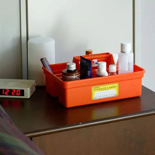 The Hightide Penco Storage Caddy in orange is a plastic organizer featuring a handle and multiple compartments to help keep your desk tidy. It also includes a yellow label affixed to the front.