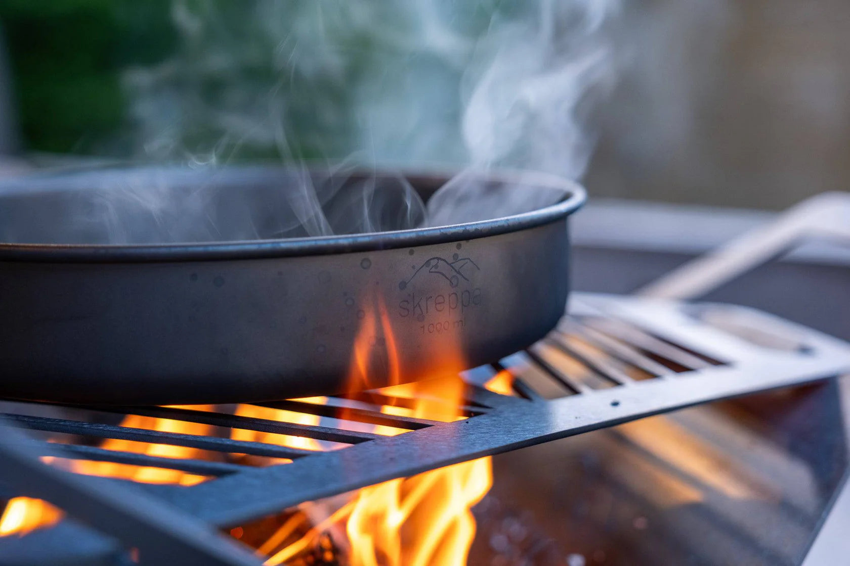 Skreppa Titanium Frying Pan over open flame, ultralight camping cookware with smoke rising for outdoor cooking.