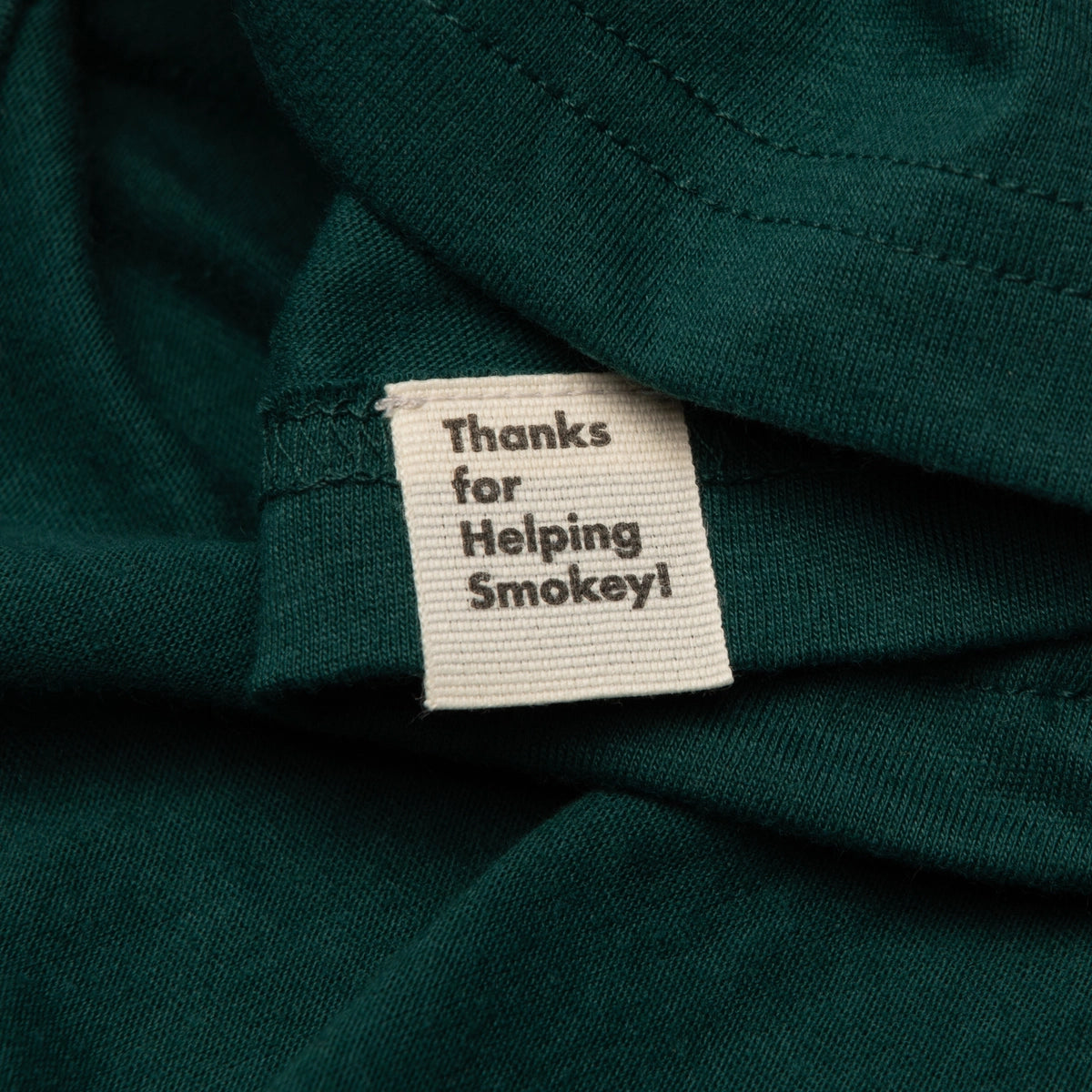 The Landmark Project Ringer Smokey Bear T-Shirt in Spruce showcases a green retro style with yellow trim, featuring an illustration of Smokey Bear wearing a hat, surrounded by trees and animals, and accompanied by text.
