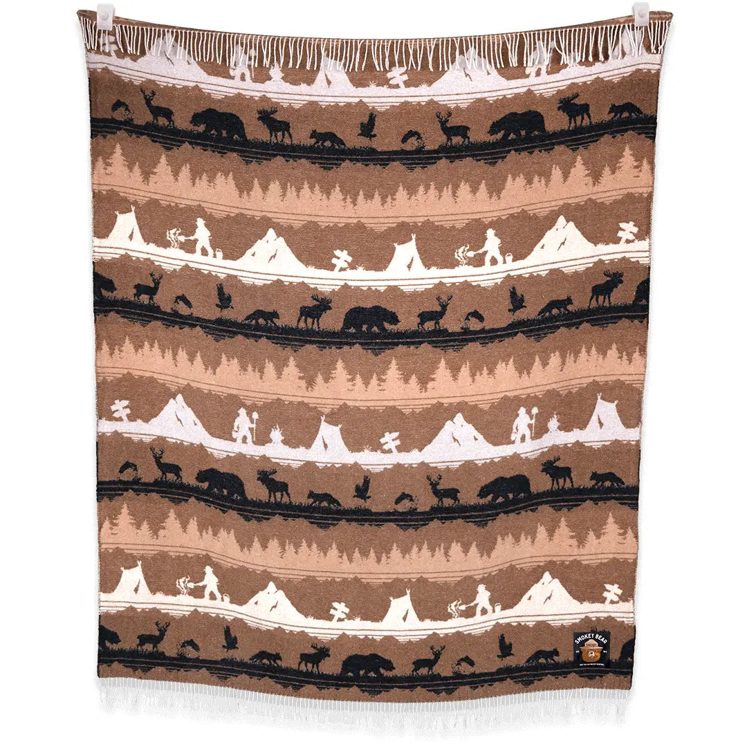 The Sackcloth & Ashes Smokey Bear Blanket - Smokey Roam is a woven masterpiece adorned with rows of nature scenes, including mountains, wildlife, and hikers. It showcases earthy tones of brown, tan, and black while promoting wildfire prevention through iconic Smokey Bear imagery.