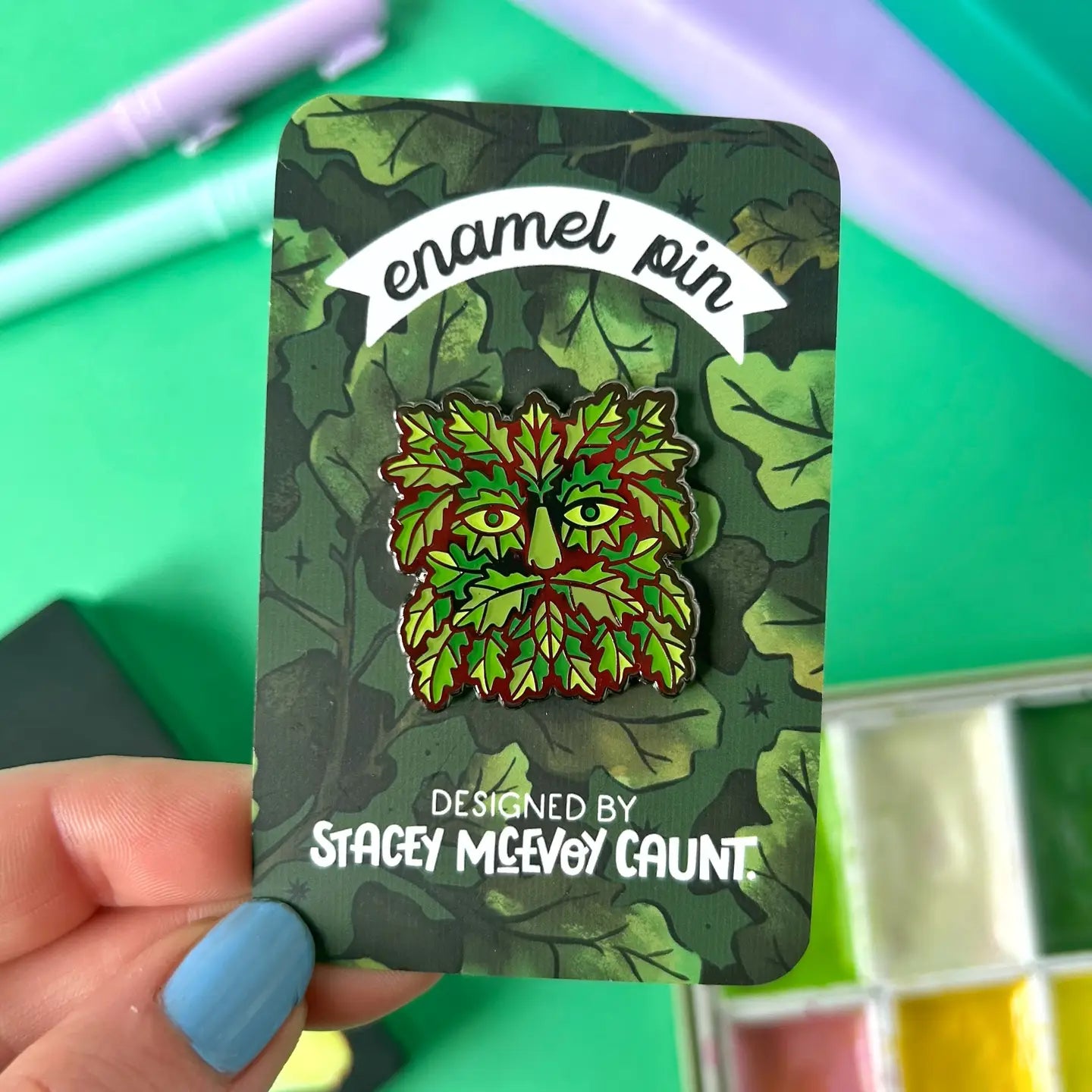 Hand holding Stacey McEvoy Caunt Green Man enamel pin, detailed with leaves. Perfect eco-friendly gift for nature enthusiasts.