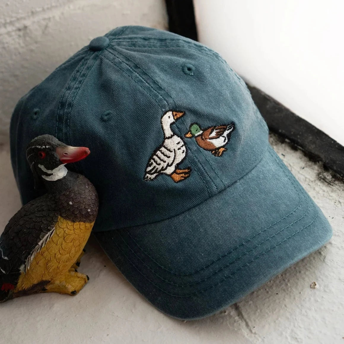 Stay Home Club Fowl Dad Cap in vintage teal next to duck figurine on white surface, stylish hat accessory, trendy cap display.