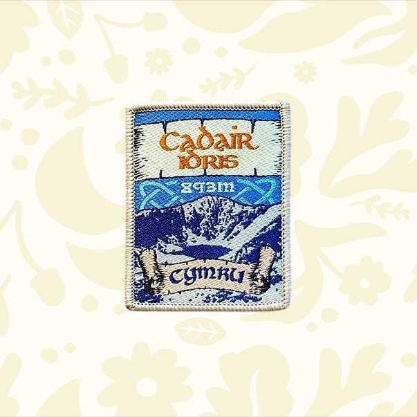Cadair Idris Patch by Adventure Patch Company, Welsh myth design, rectangular patch on rustic wood background, hiking souvenir.