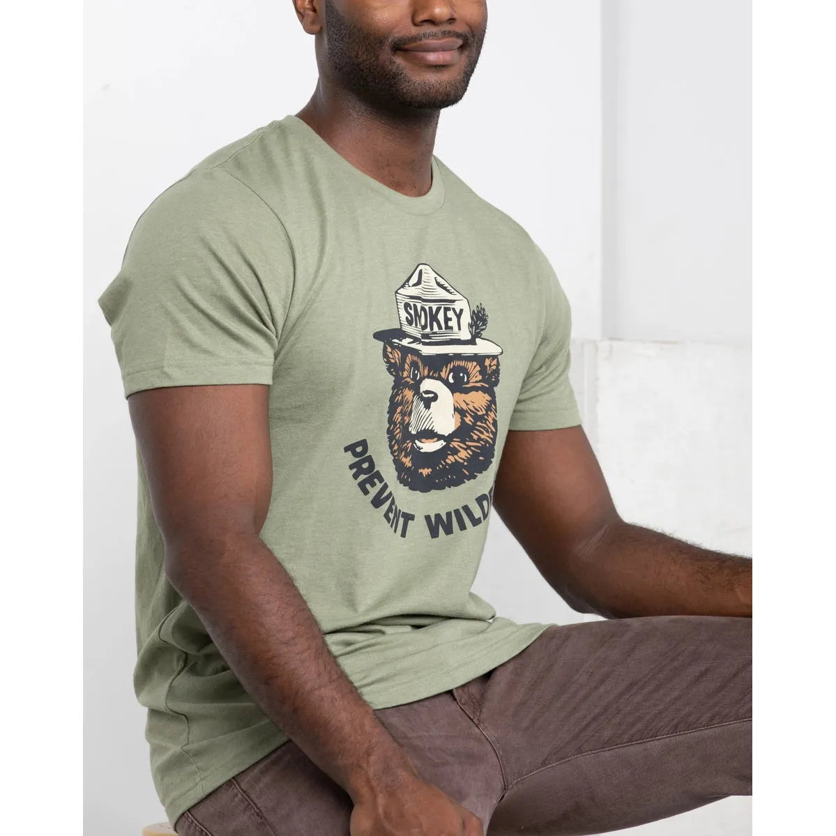 Discover the allure of our cactus green Landmark Project Retro Smokey Bear T-Shirt, showcasing a graphic of a bear in a ranger hat with "Smokey" text and the phrase "Prevent Wildfires" in vintage colors. This sustainably crafted T-shirt seamlessly combines style and purpose.