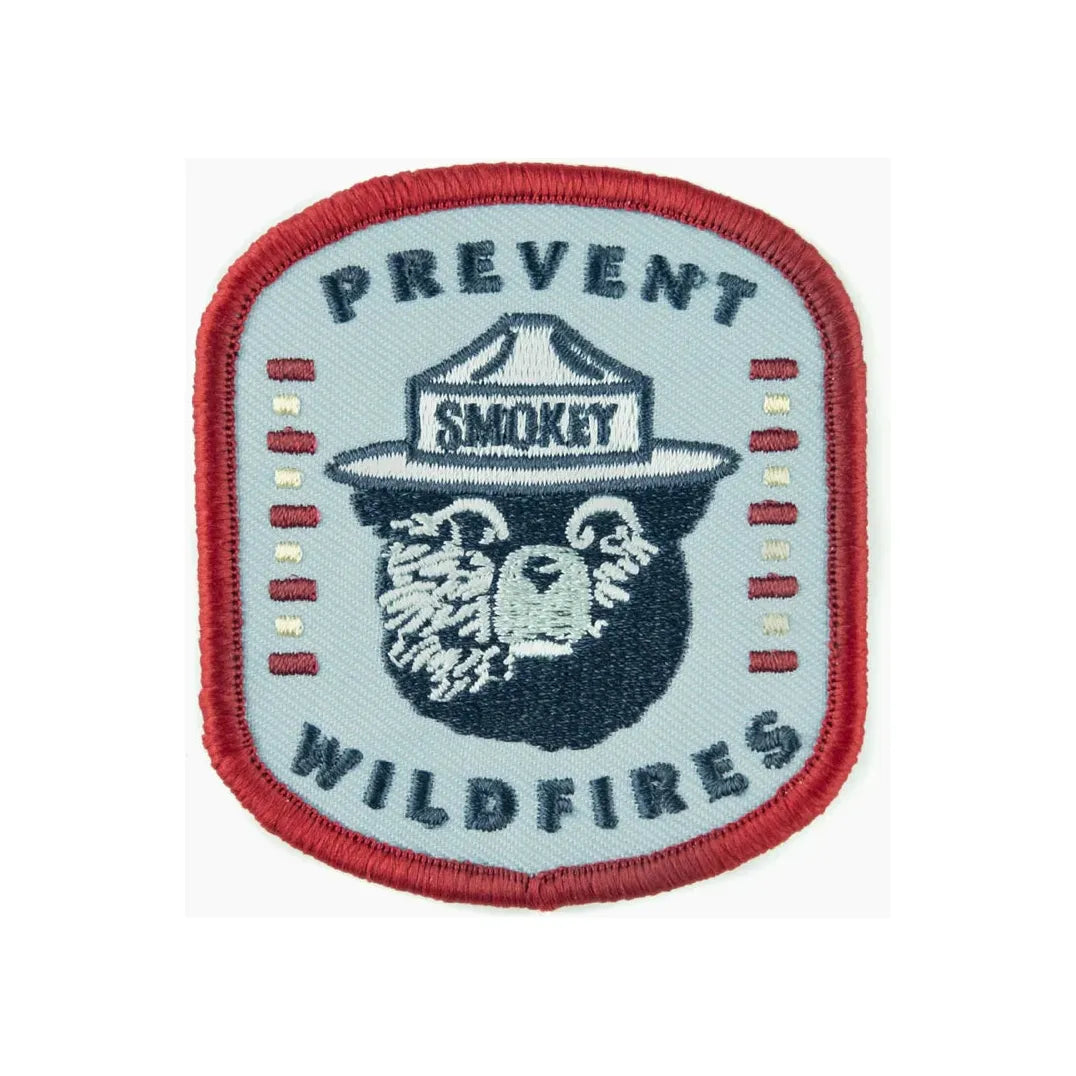 An embroidered iron-on patch, The Landmark Project Smokey Bear Patch - Iconic Prevent Wildfires, features a bear wearing a ranger hat that reads "Smokey," surrounded by the text "Prevent Wildfires." Perfect for outdoor adventures, this patch comes in sustainable packaging.