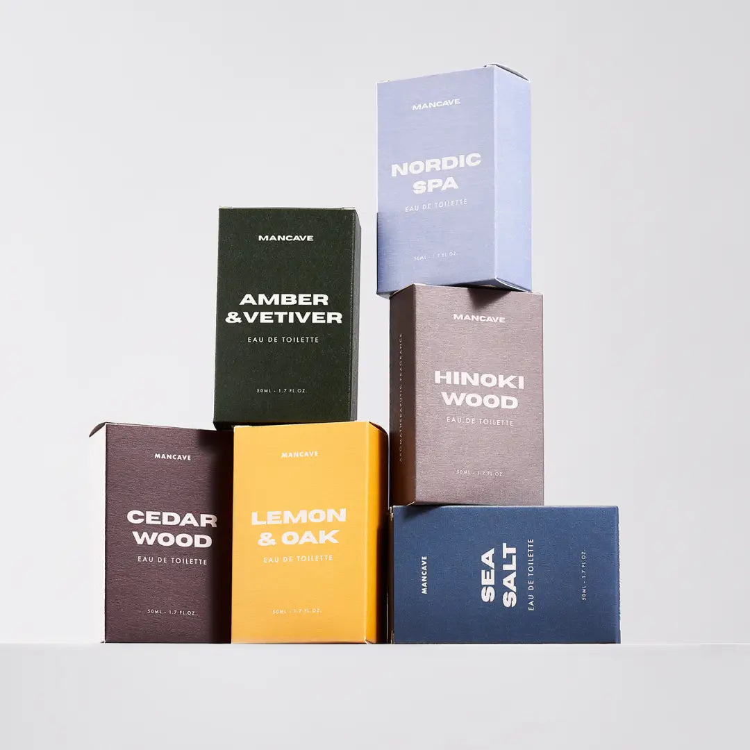Six ManCave Hinoki Wood Eau De Toilette bottles in a pyramid, each showcasing a distinct woody fragrance on a light backdrop.