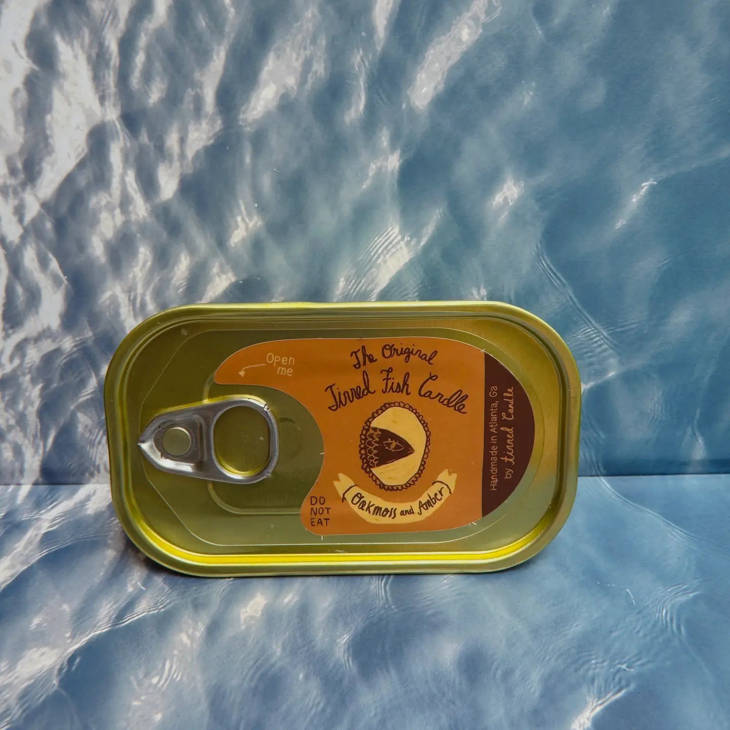 The Original Tinned Fish Candle Oakmoss & Amber by Tinned Candle displayed on blue marbled surface, home decor accent, gift idea.