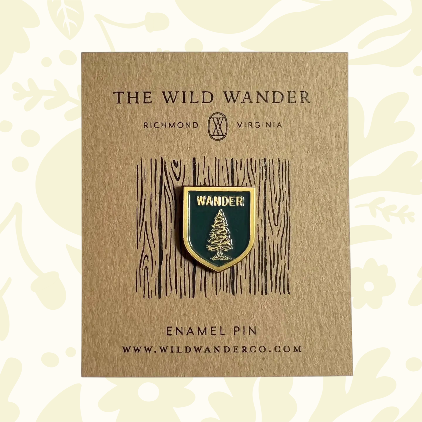 Green enamel pin with fir tree, WANDER text, on The Wild Wanders branded card—forest nature hiking accessory.