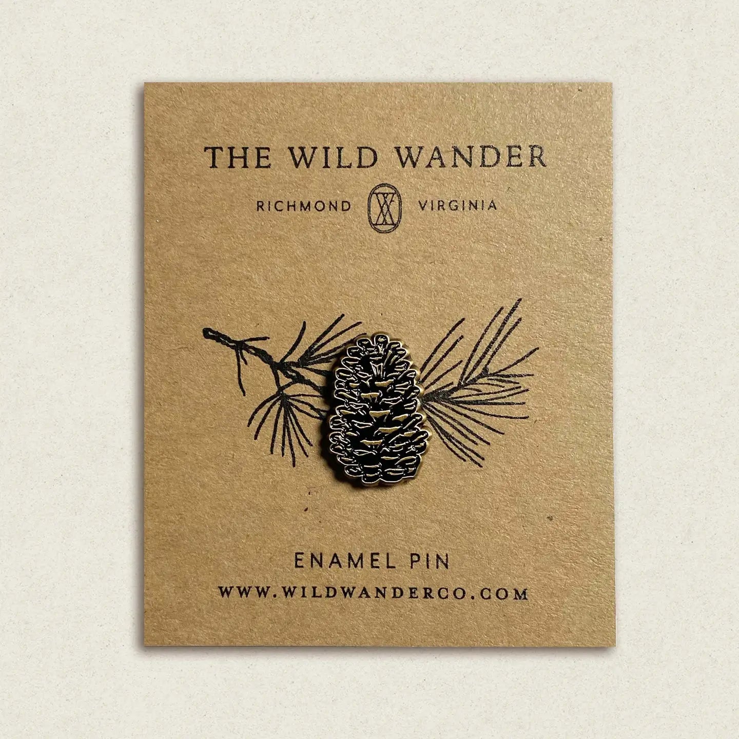 The Wild Wander Pine Cone Enamel Pin on branded brown card; nature-inspired accessory from The Wild Wander collection.