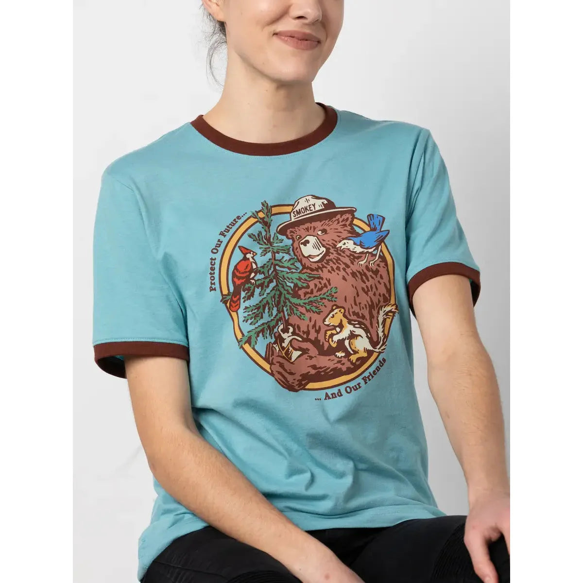 Person wearing a blue The Landmark Project Ringer Smokey Bear T-Shirt - Glacier featuring Smokey Bear with woodland animals and text saying, "Protect Our Nature ...And Our Friends."
