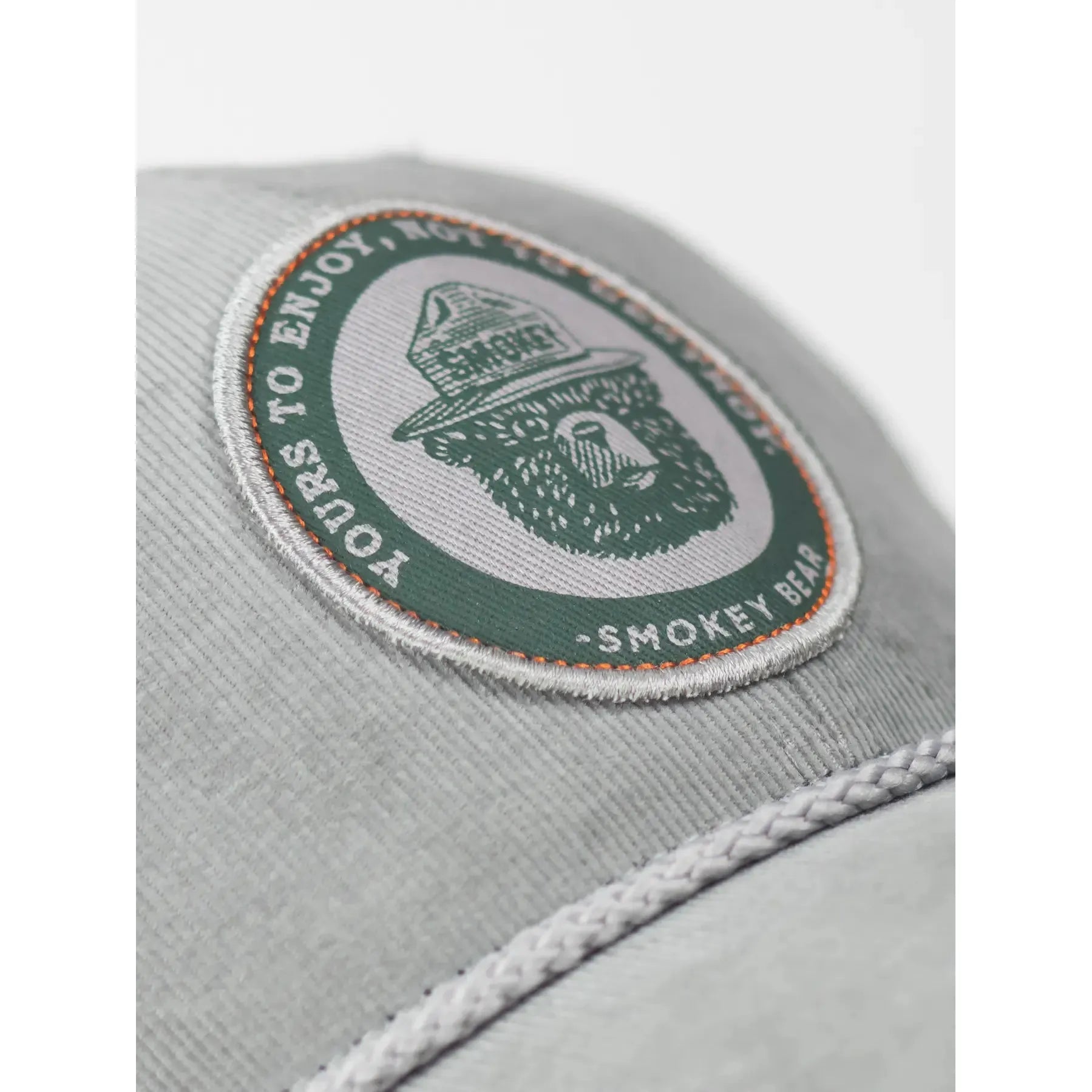 The Landmark Project Yours To Enjoy Smokey Bear Cap is a light gray baseball cap with an embroidered circular patch featuring a hat-wearing bear and the text 'Smokey Bear 'Only You.' Celebrating wildfire prevention, this cap is a must-have among Smokey Bear products endorsed by the US Forest Service.