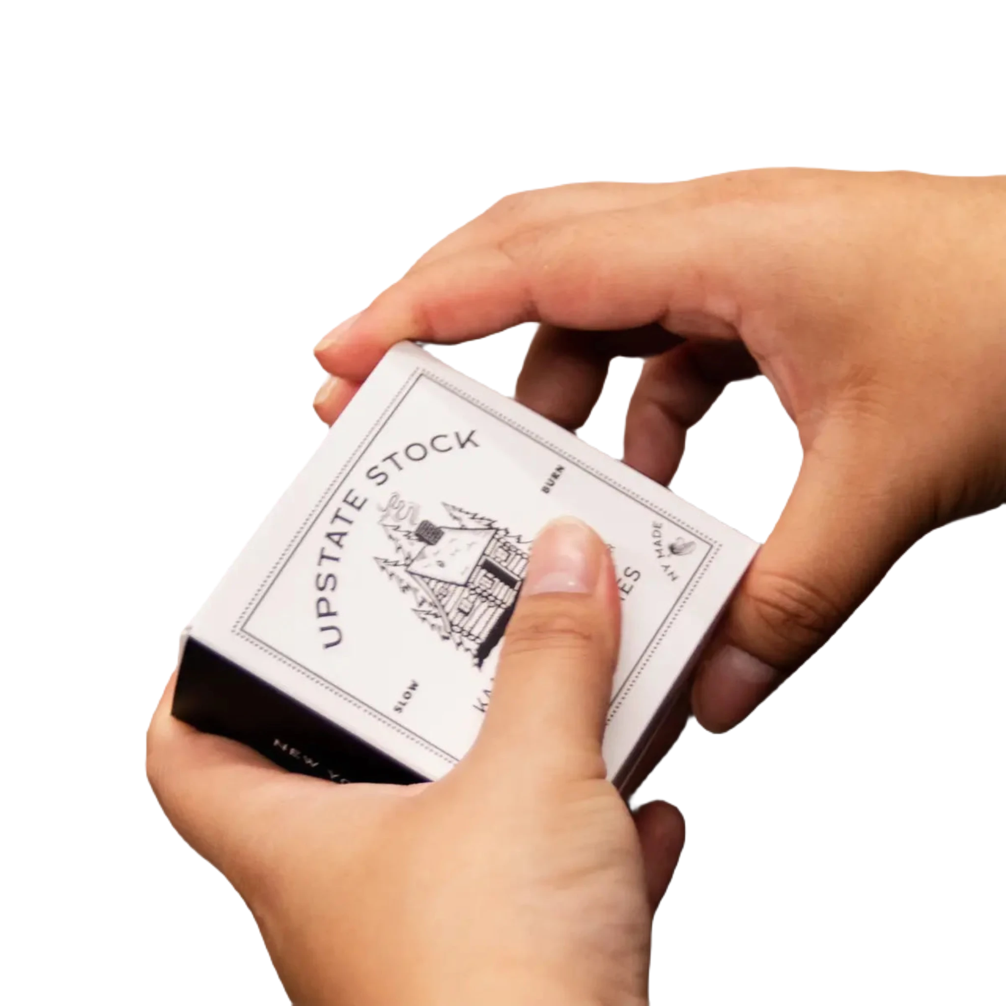 Close-up of hands holding a box labeled "Upstate Stock Kaaterskill Wilds Incense Cones" with a vintage-style illustration and text on a dark brown surface, reminiscent of the rich tones found in Kaaterskill Wilds.