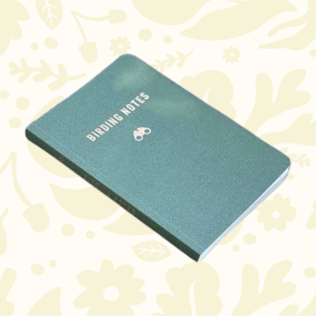 Forager Provisions LTD Birding Notes field journal with a green cover resting on a rustic wooden park bench.