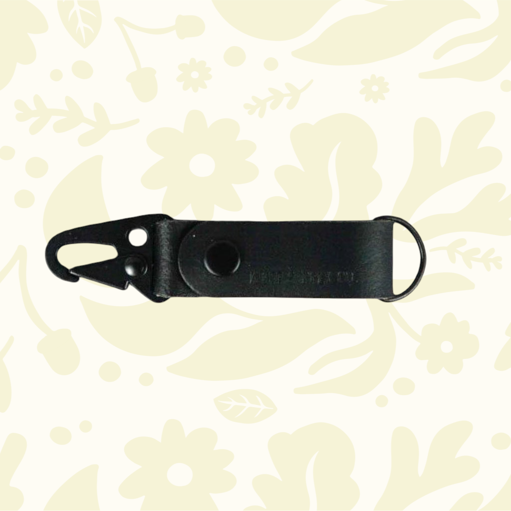 Premium Kjøtt Forager Provisions black leather key fob, full-grain leather & metal ring on cream floral background.