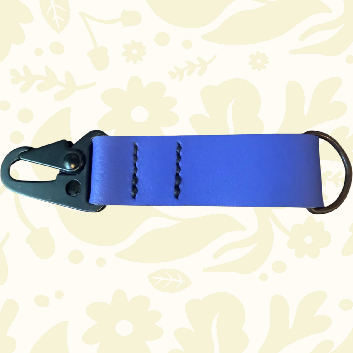 Blue Kjøtt Leather Key Fob with metal clip and D-ring displayed on light floral background, stylish keychain accessory.