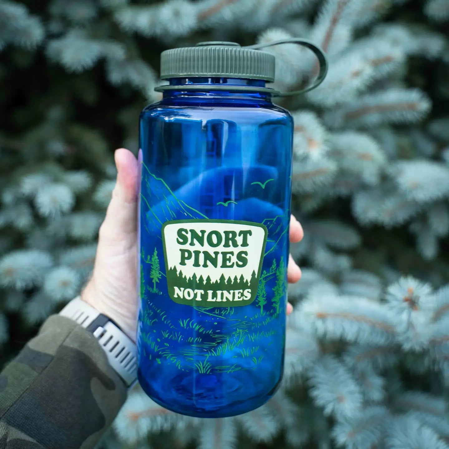 Forager Provisions LTD blue Nalgene 32oz water bottle with Snort Pines Not Lines graphic held in front of pine trees.