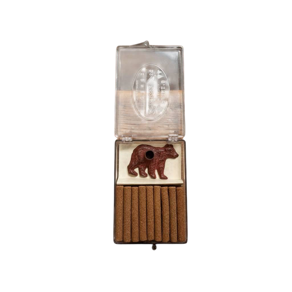 Forager Provisions LTD brass bear incense holder set with balsam fir logs in a clear plastic display case on a table.