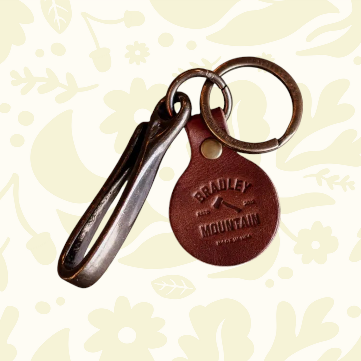 Forager Provisions LTD Bradley Mountain brass fish hook key fob with a branded leather tag on a patterned background.