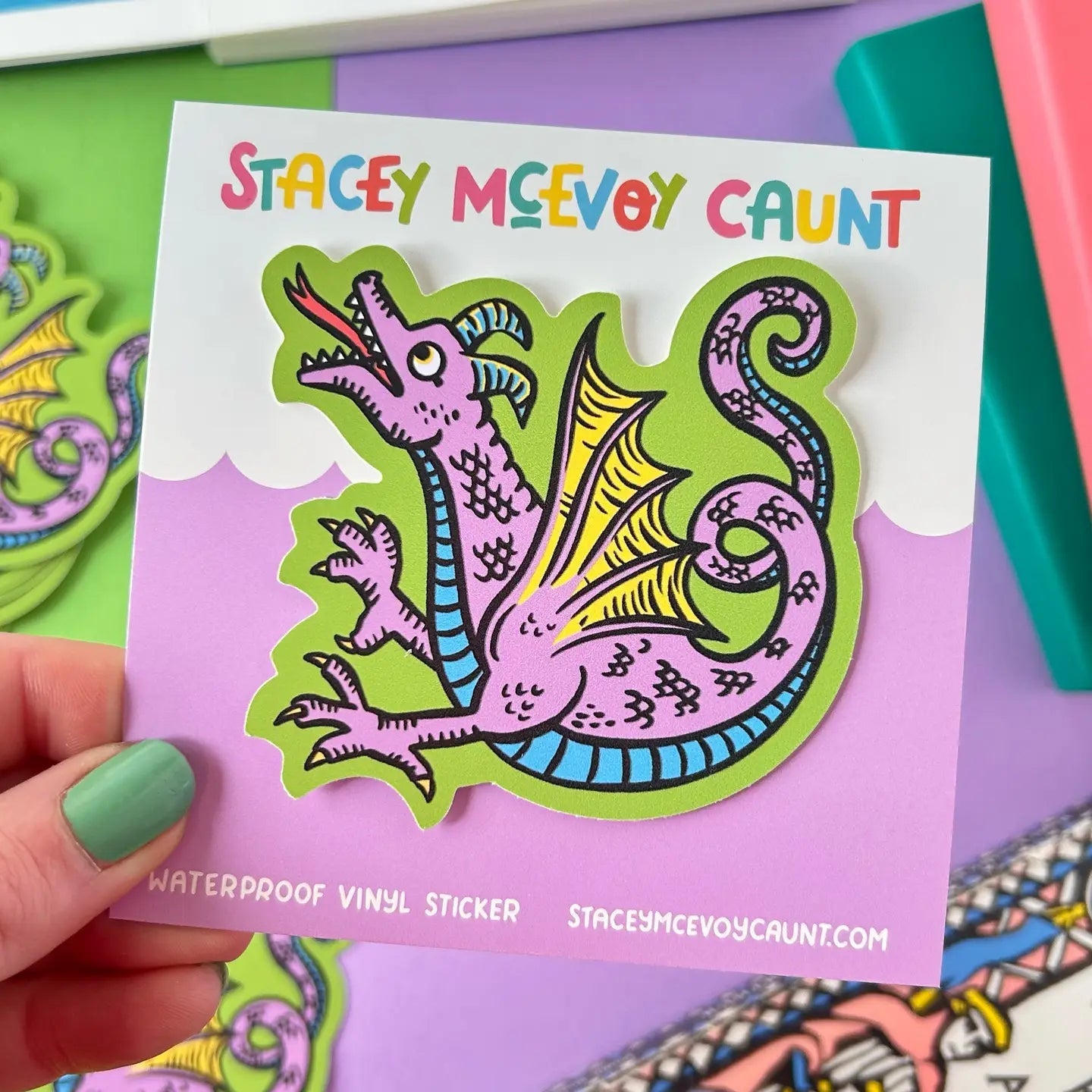 Hand holding Stacey McEvoy Caunt Dragon Medieval Marginalia Vinyl Sticker on branded card—unique fantasy art accessory.
