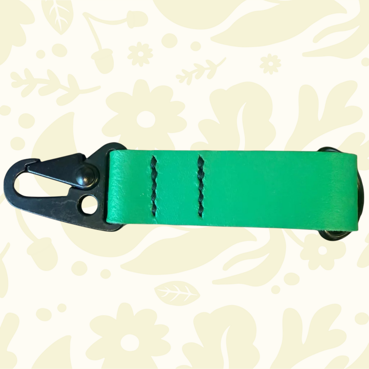 Kjøtt Supply Co green leather key fob with black stitching, metal clip, on floral background. Forager Provisions accessory.