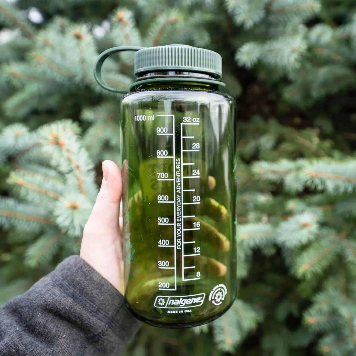 Forager Provisions LTD green 32oz Nalgene wide-mouth water bottle with measurement markings held against pine trees