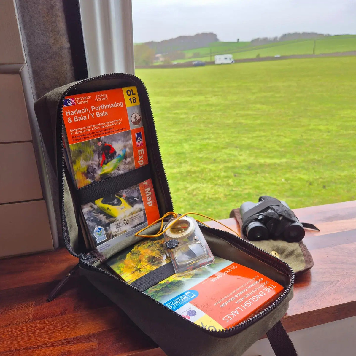 Forager Provisions LTD green waxed canvas map case open on a windowsill containing OS maps and a compass