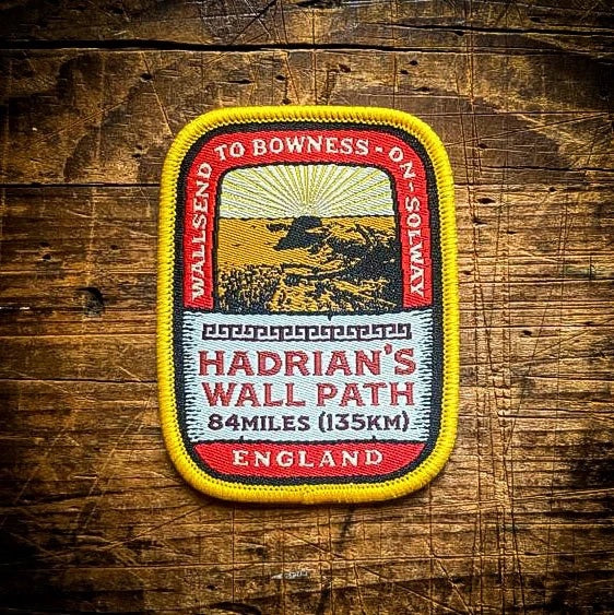 Forager Provisions LTD embroidered Hadrian's Wall Path patch with Roman ruins design on a rustic wooden background.