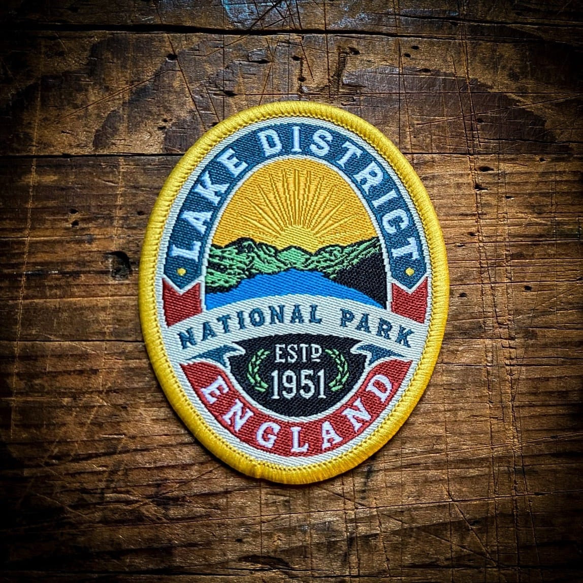 Forager Provisions LTD embroidered Lake District National Park patch with hills, lake, and sun on a wooden background.