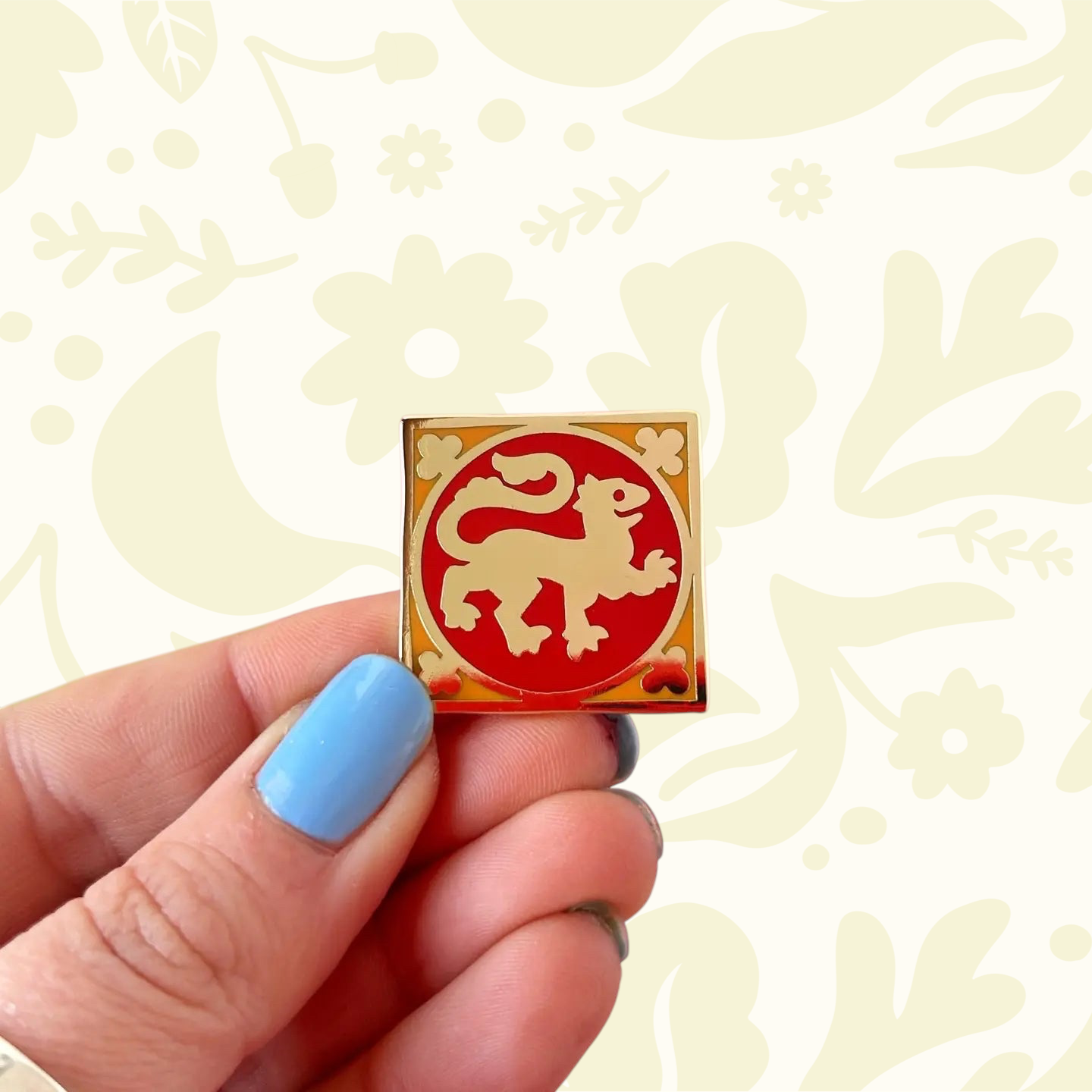 Forager Provisions LTD enamel pin featuring a red and gold square lion medieval tile design held in a hand.