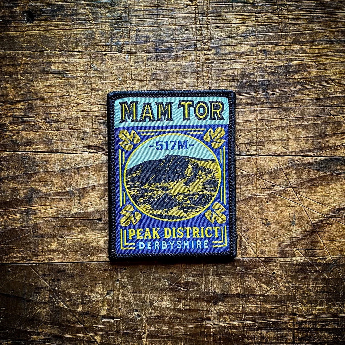 Forager Provisions LTD Mam Tor embroidered patch featuring a mountain landscape design on a rustic wooden background.