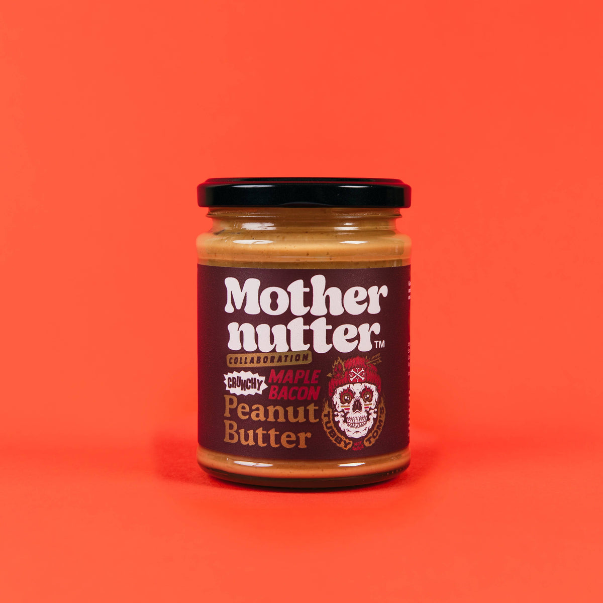Forager Provisions LTD Mothernutter crunchy maple bacon peanut butter in a glass jar against a bright orange background.
