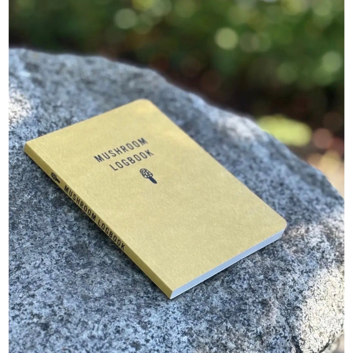 Forager Provisions LTD Mushroom Logbook field journal with a yellow cover resting on a textured grey forest rock
