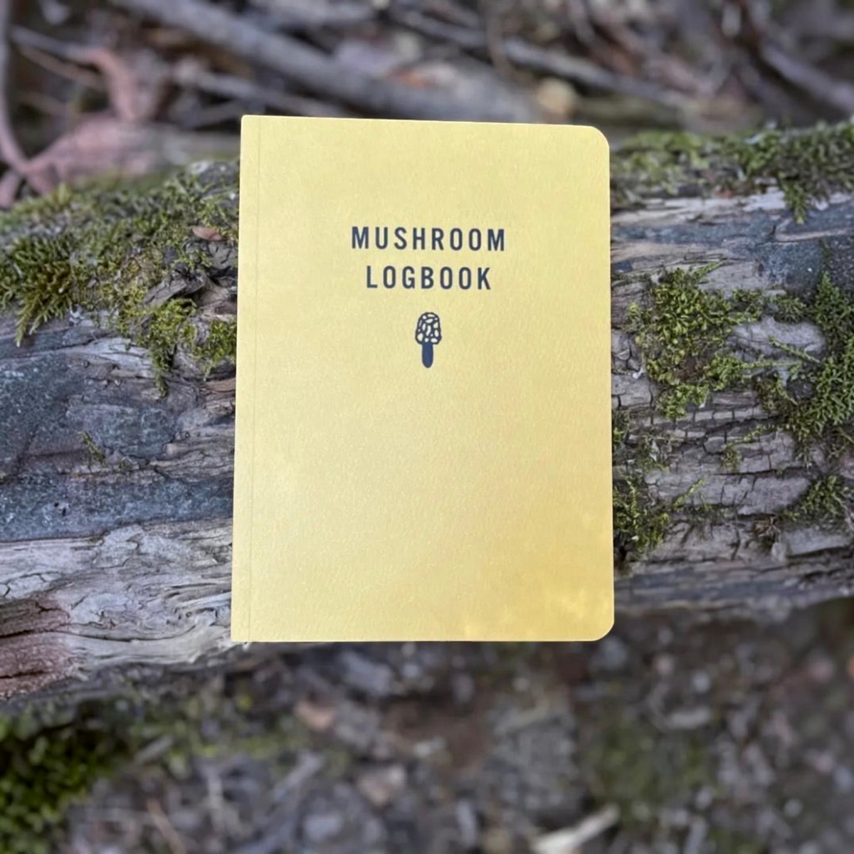 Forager Provisions LTD Mushroom Logbook with a yellow cover resting on a mossy forest log