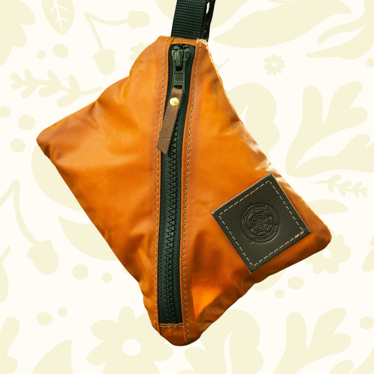 Forager Provisions LTD Journeyman Handcraft orange waxed canvas X-Pouch with a diagonal zip closure hanging outdoors