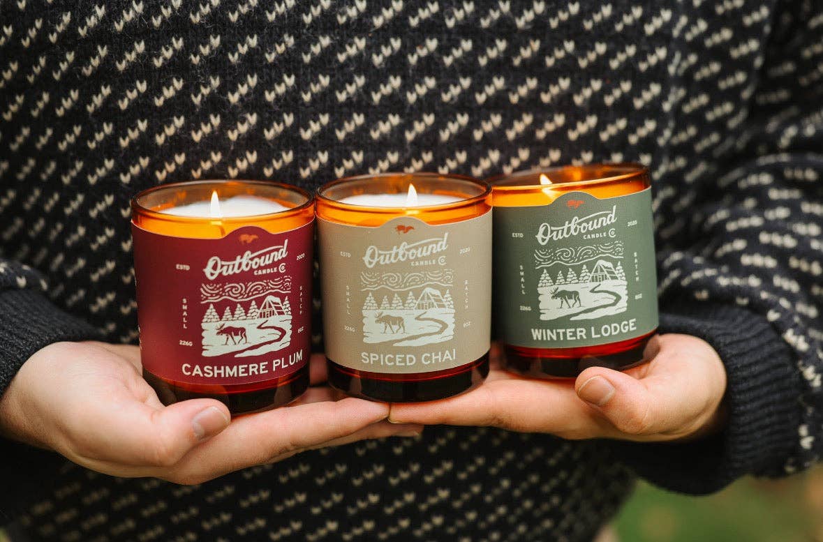 Forager Provisions LTD features three Outbound Candle Co soy candles in amber glass jars held against a knit sweater.