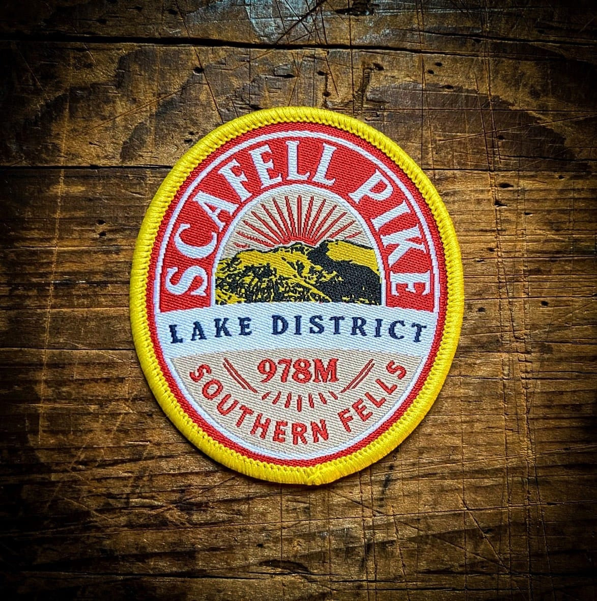 Forager Provisions LTD embroidered Scafell Pike patch with red, yellow, and white mountain design on wood background.