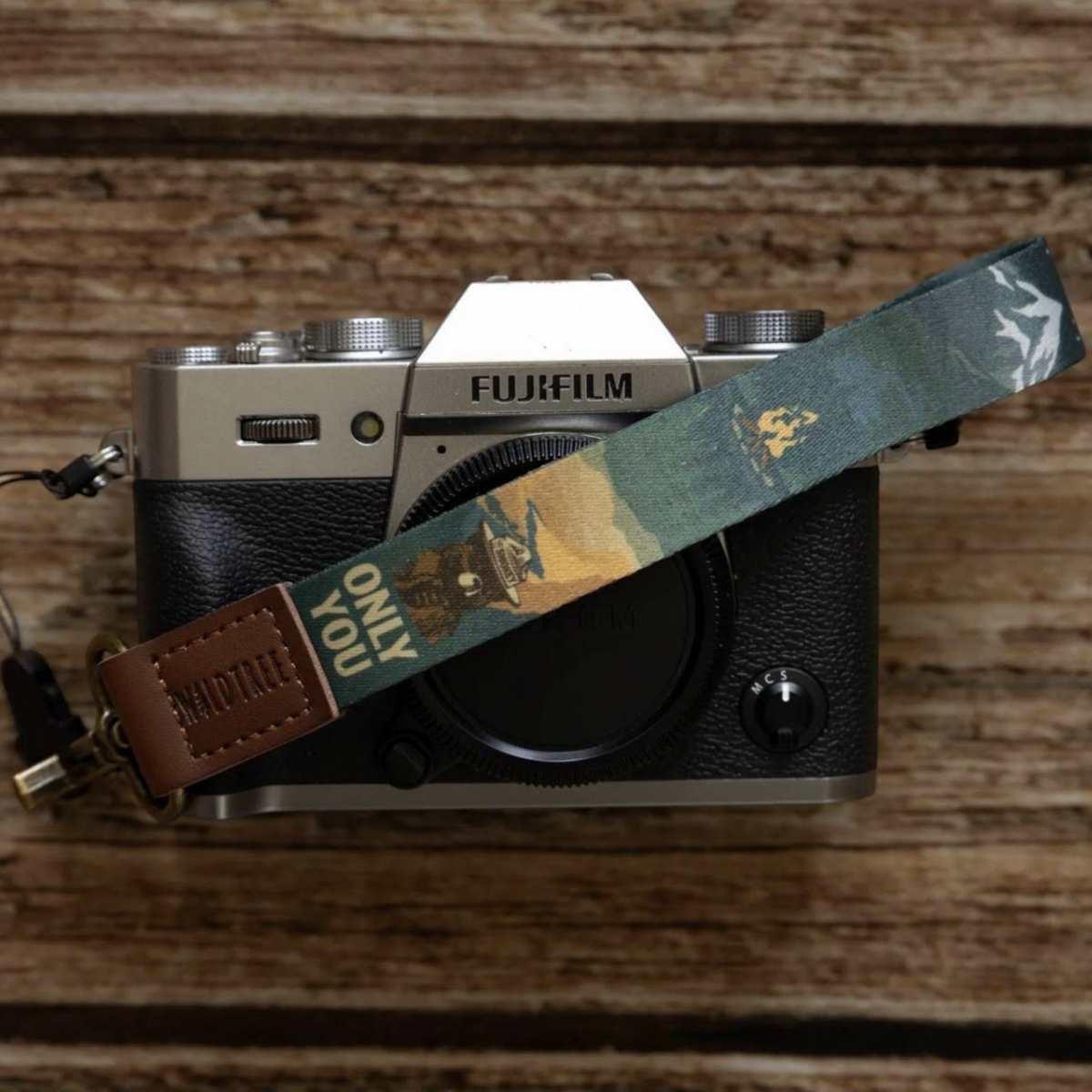 Fujifilm camera on wooden table, featuring Wildtree Smokey Bear wrist keychain—best camera gear accessories display.