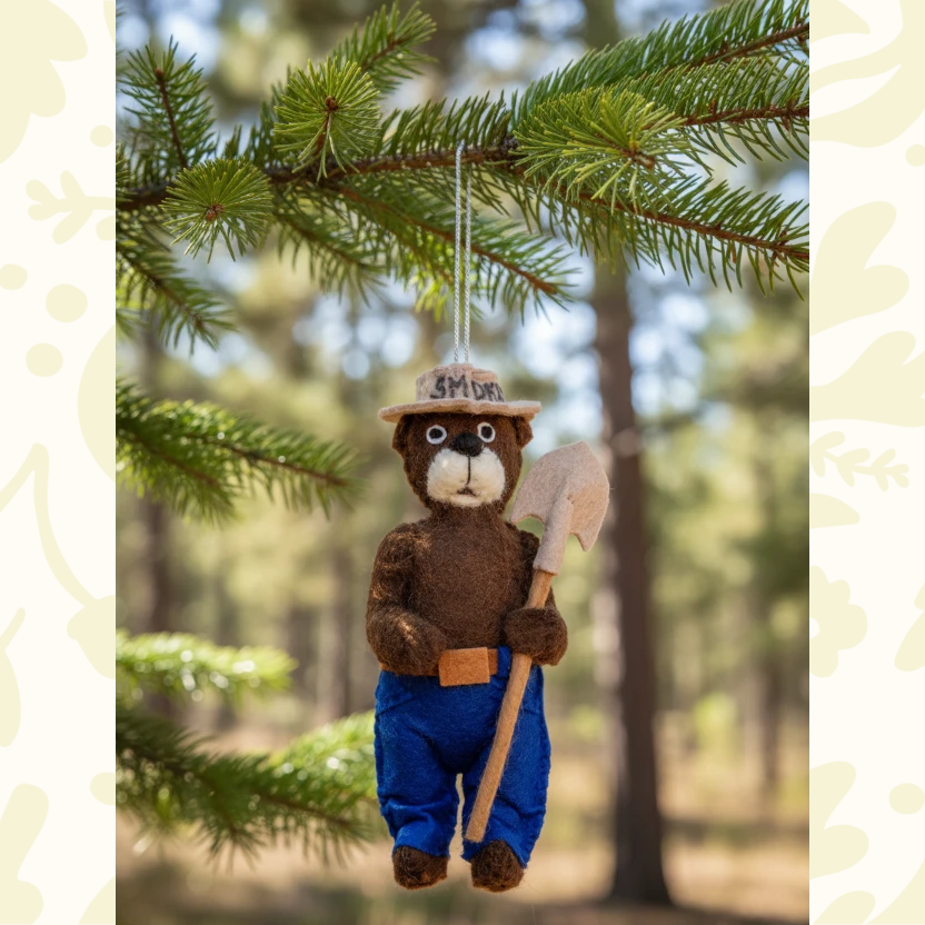 Forager Provisions LTD handmade felt Smokey Bear ornament hanging from a pine branch with a shovel and ranger hat.