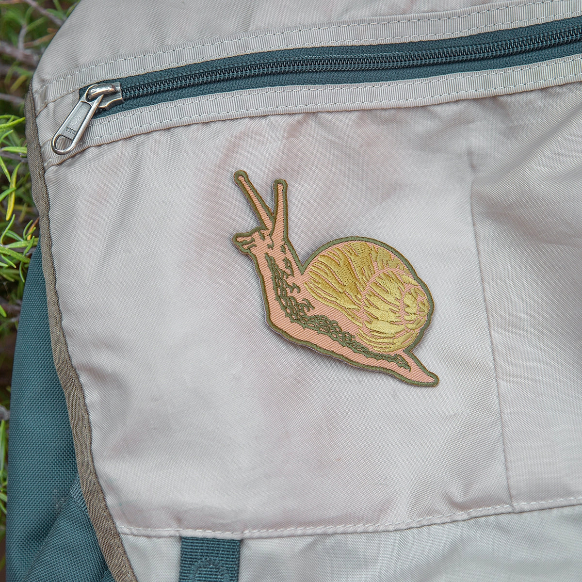 Forager Provisions LTD Mustard Beetle embroidered snail iron-on patch attached to a beige canvas backpack