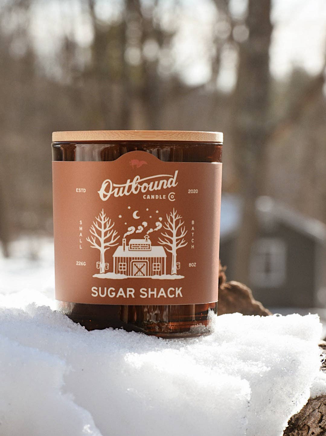 Forager Provisions LTD Outbound Candle Co Sugar Shack soy candle with bamboo lid in a snowy woodland setting