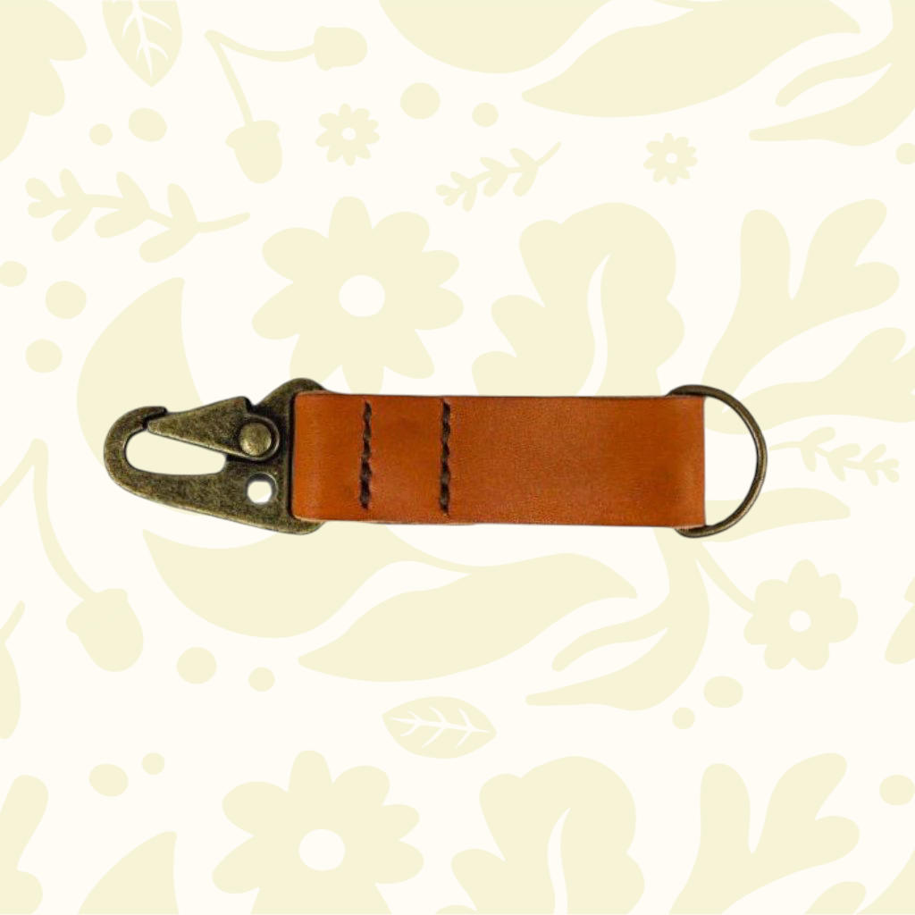 Brown Kjøtt Forager Provisions leather key fob with metal clasp on beige floral background; premium key accessory.