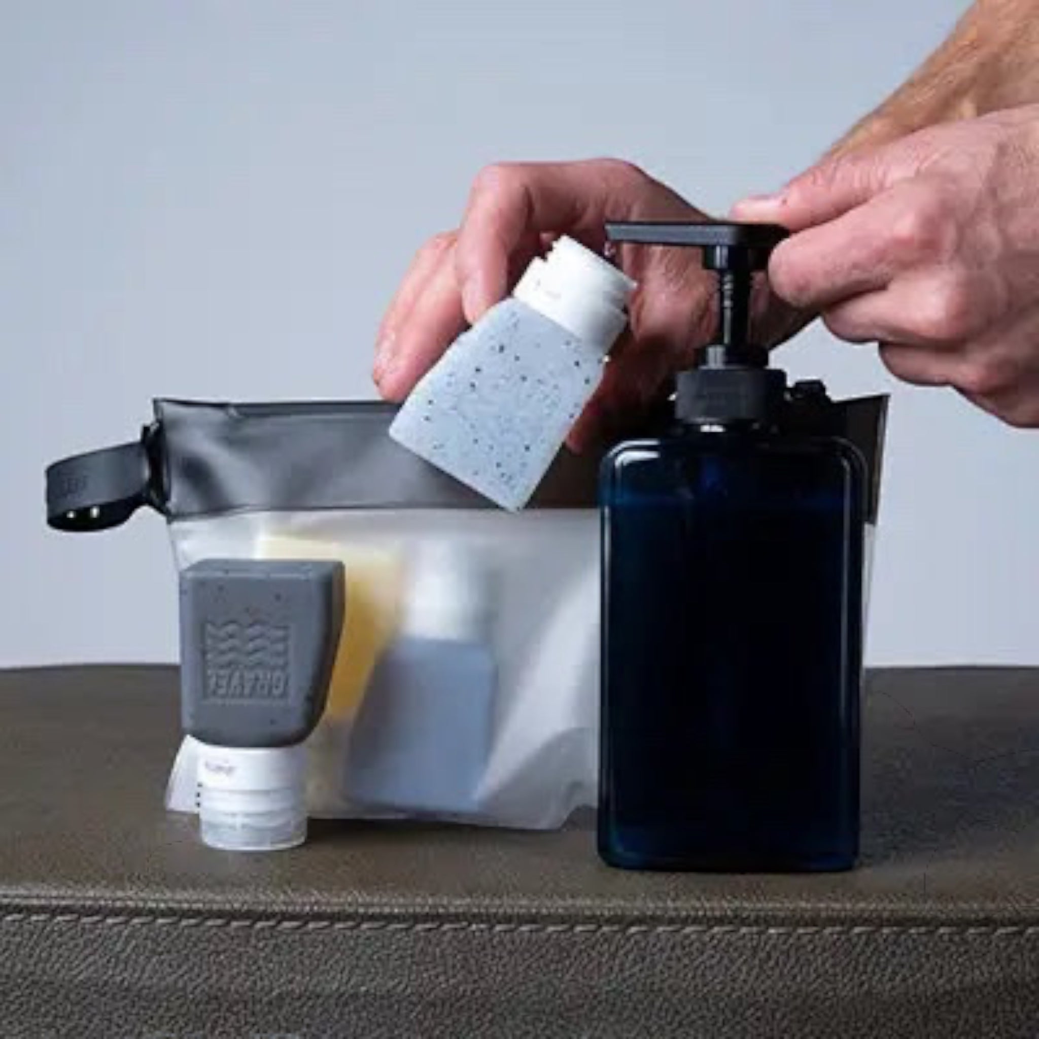 Forager Provisions LTD Gravel Outdoors travel bottles being filled from a pump dispenser into a toiletry bag.