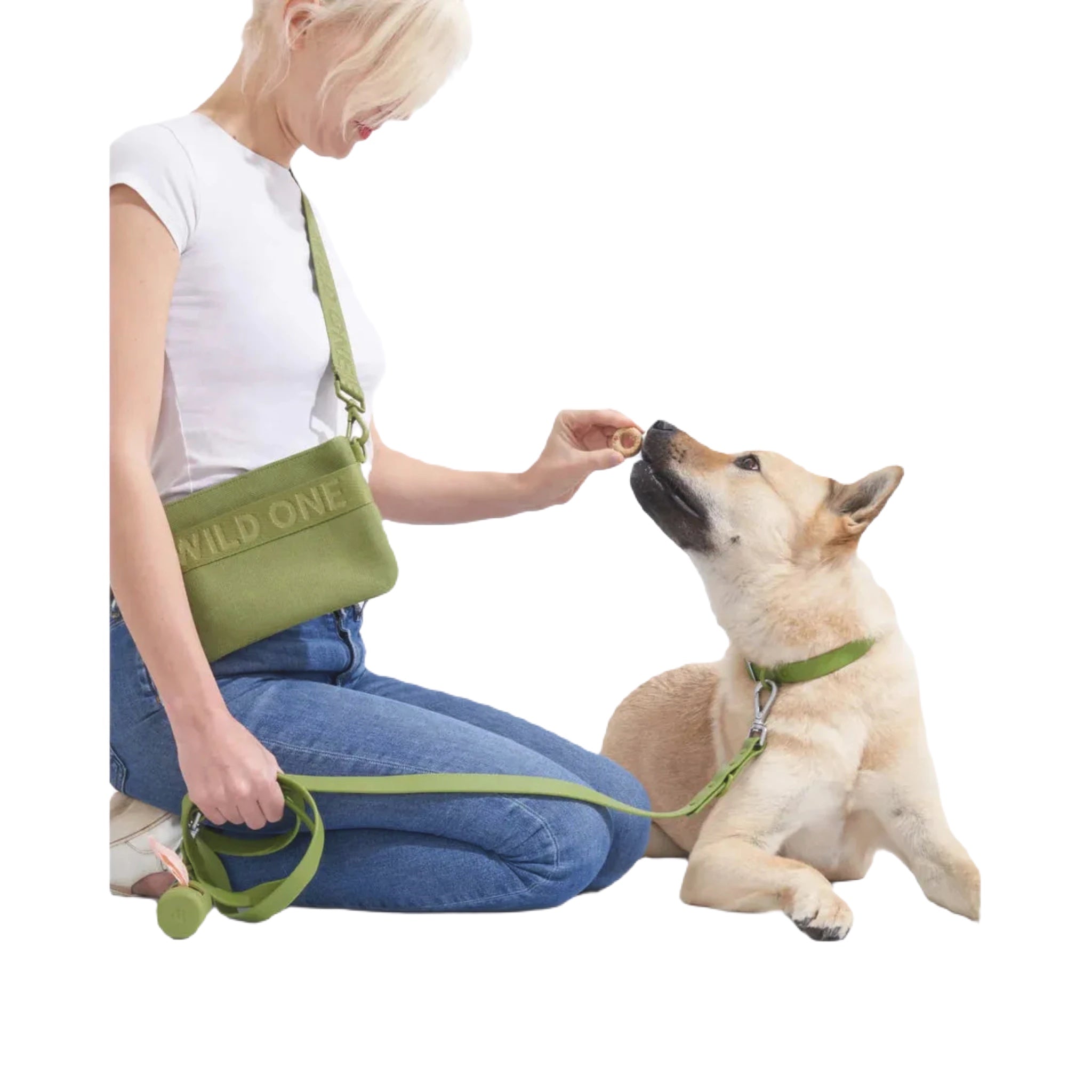 Person treats a tan dog on a green Wild One leash with Moss Poop Bag Holder; pet gear, dog walking essentials visible.