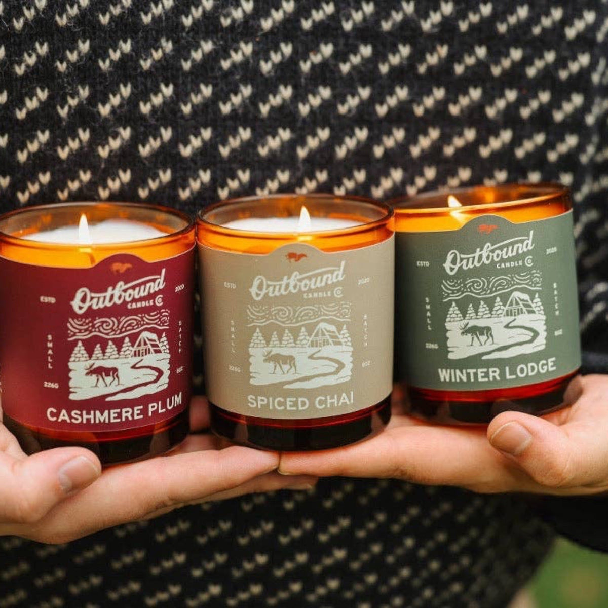 Forager Provisions LTD Winter Lodge soy candle trio with festive labels held in hands against a knit sweater background