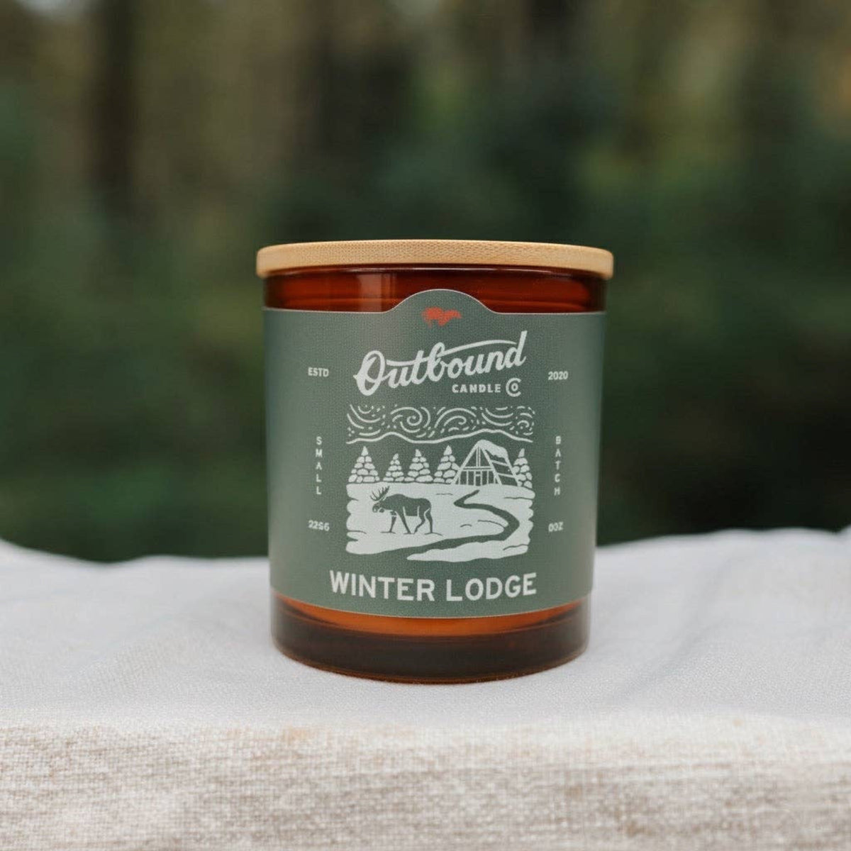 Forager Provisions LTD Winter Lodge soy candle in an amber glass jar with a bamboo lid and winter-themed label.