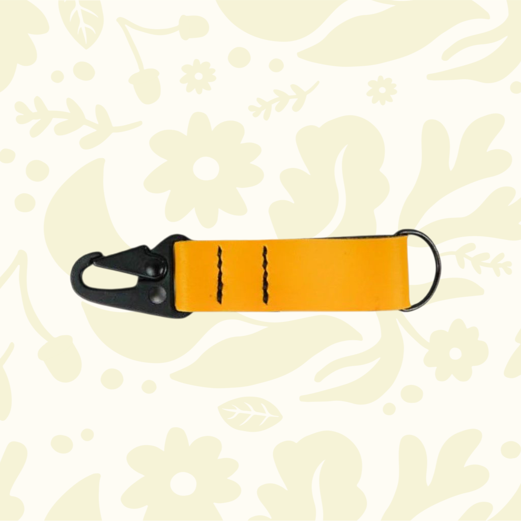 Kjøtt Forager Provisions yellow leather key fob with black clip, displayed on a vibrant floral background for style.